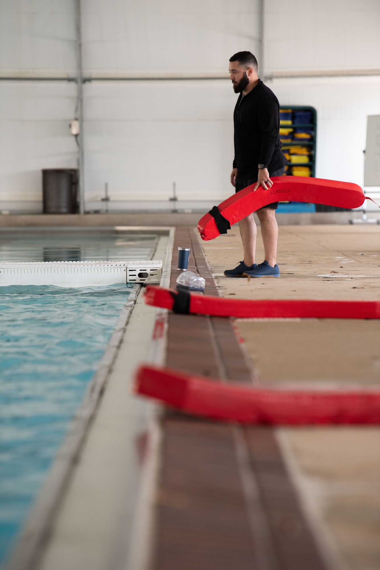 man stands next to pool holding lifeguard floatation device
