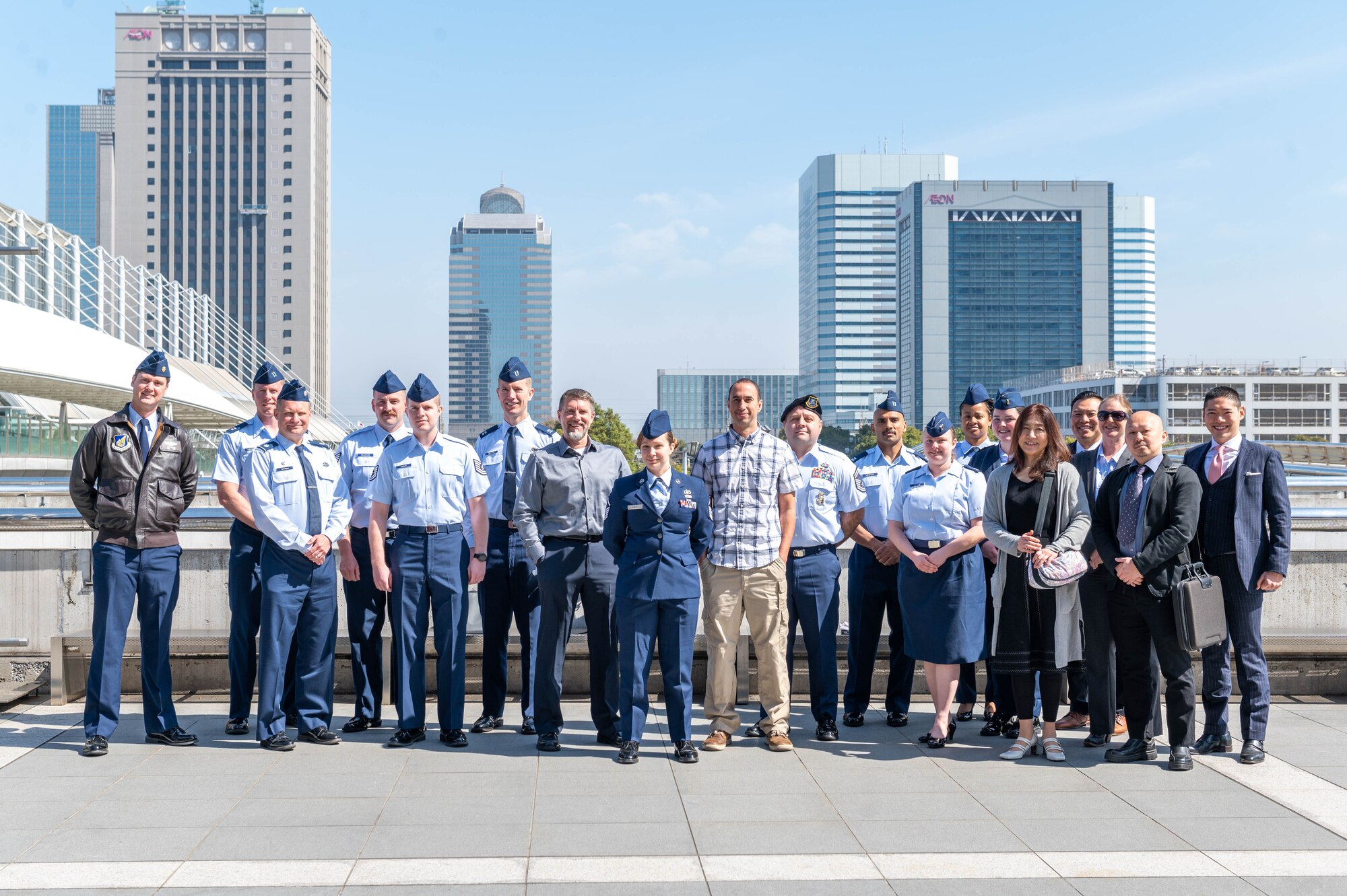 Nineteen people pose for a group photo with the Tokyo skyline in the background.