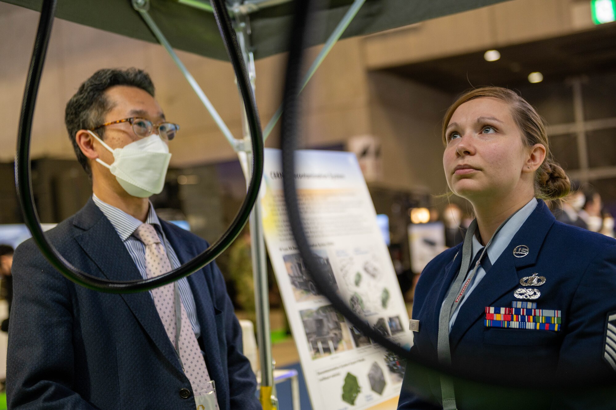A white woman stands next to a Japanese man beneath a tent.