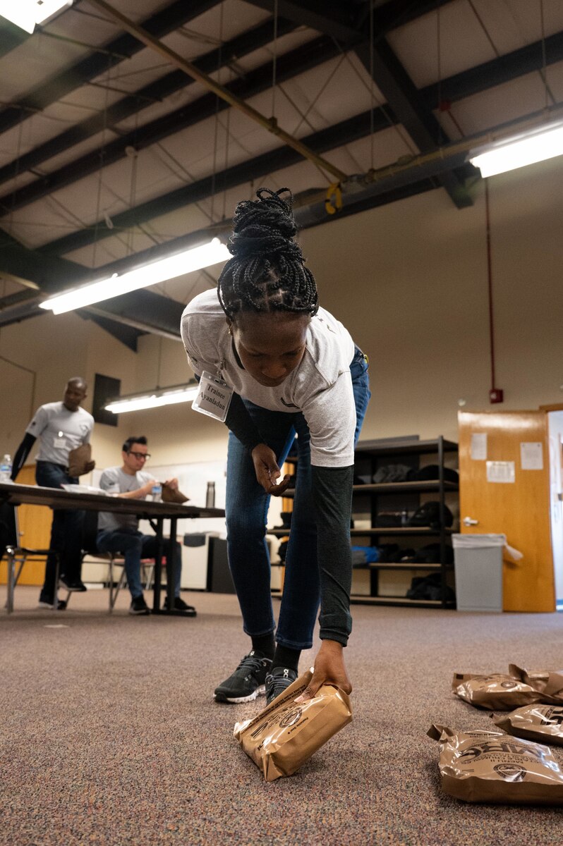 Trainee Dorcas Ayanladun, 934th Airlift Wing Development and Training Flight trainee, selects a meal ready-to-eat from a pile on the floor of the D&TF building at the Minneapolis-St. Paul Air Reserve Station, Minnesota, March 5, 2023. Dorcas enlisted to work in personnel management after completing her initial entry training. (U.S. Air Force photo by Senior Airman Victoriya Tarakanova)