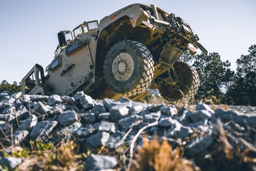 A large military vehicle is driven over a pile of rocks and turf.