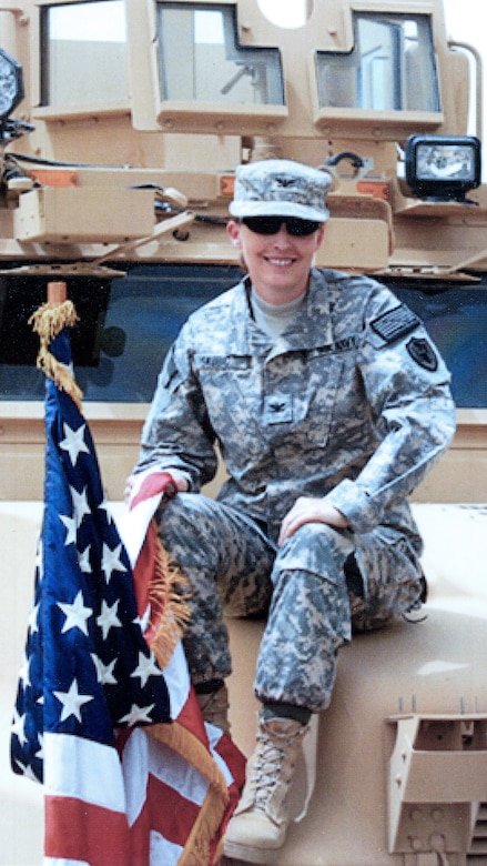 A uniformed service member sits on the hood of a military vehicle.