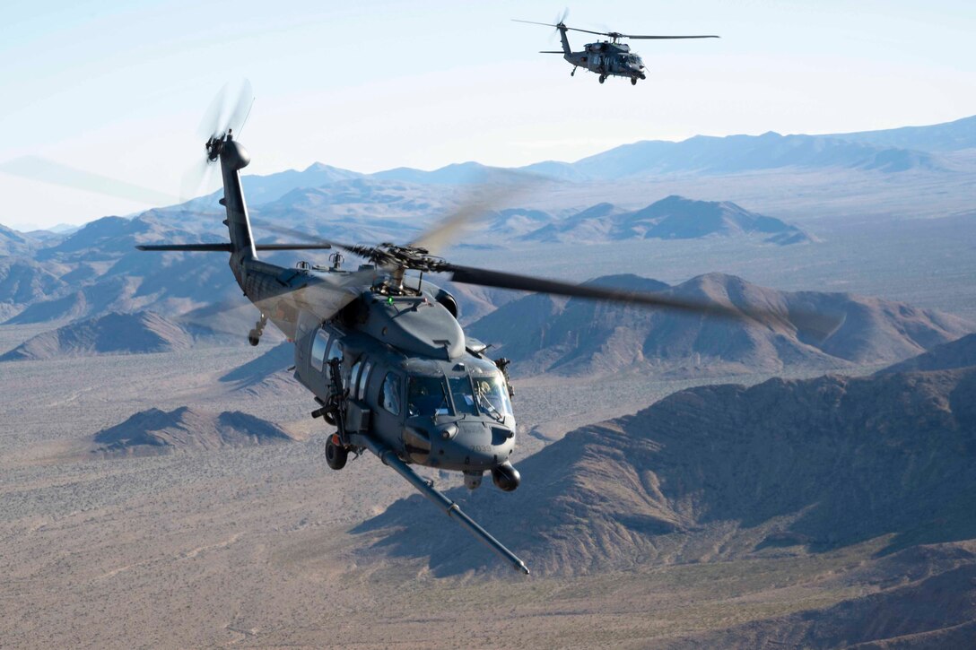 Two helicopters fly over a mountain range.