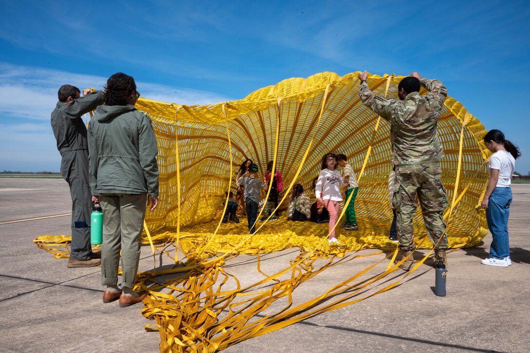 Children play inside a military parachute as airmen hold up one side.