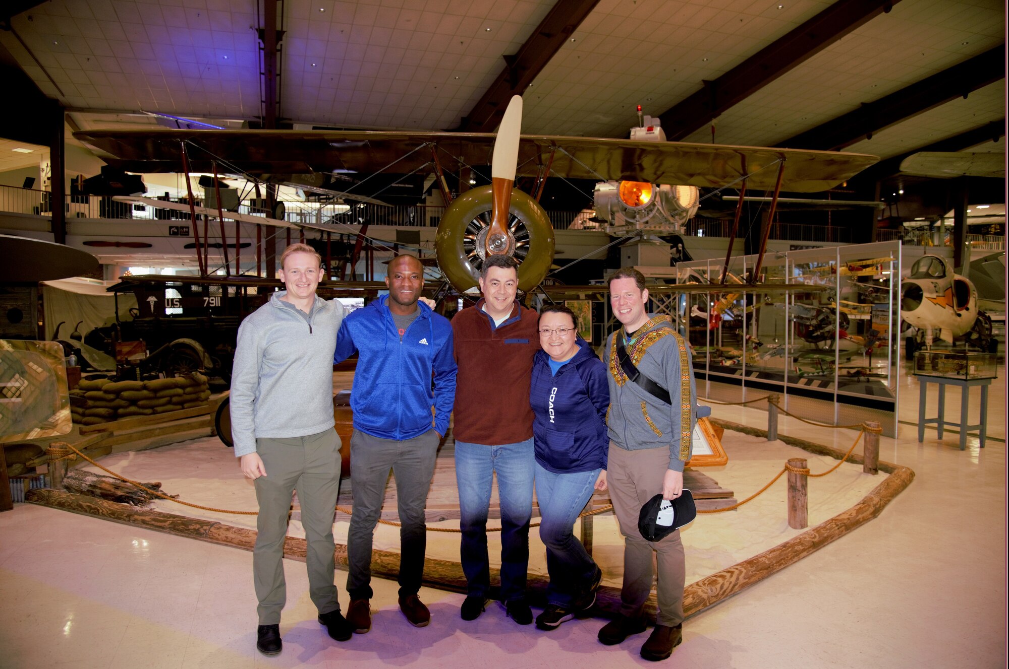 plain clothes military members posing for photo in front of aircraft