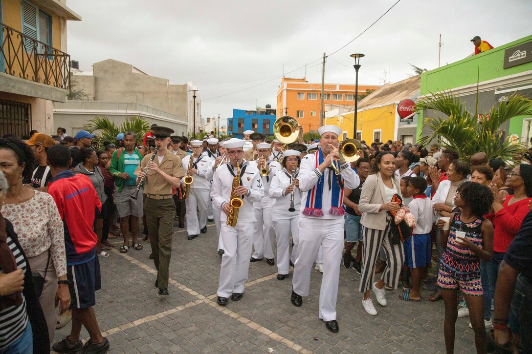 U.S. Marines and sailors play instruments in the middle of crowds in a street in Cape Verde.
