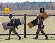 Men in U.S. Army uniforms carrying pistol targets outdoors.