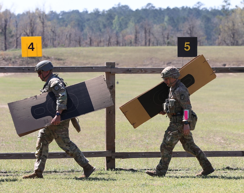 Men in U.S. Army uniforms carrying pistol targets outdoors.