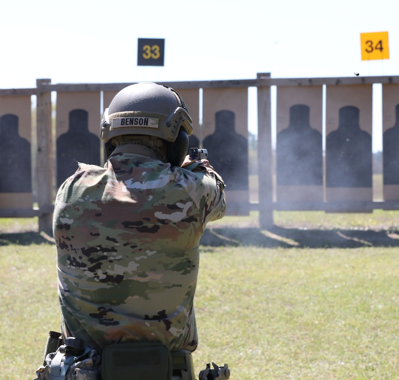 Man in US Army uniform firing pistol on outdoor pistol range.