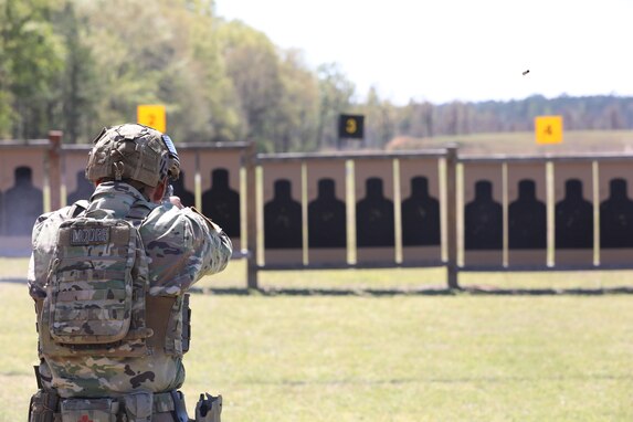 Man in US Army uniform firing pistol on outdoor pistol range.