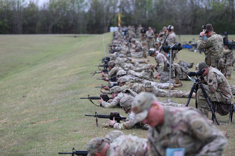 Multiple men in U.S. Army uniforms on outdoor rifle range.