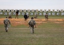 Men in U.S. Army uniform walk up to the next firing position outdoors.