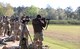 Multiple men in U.S. Army uniforms fining rifles on outdoor rifle range.