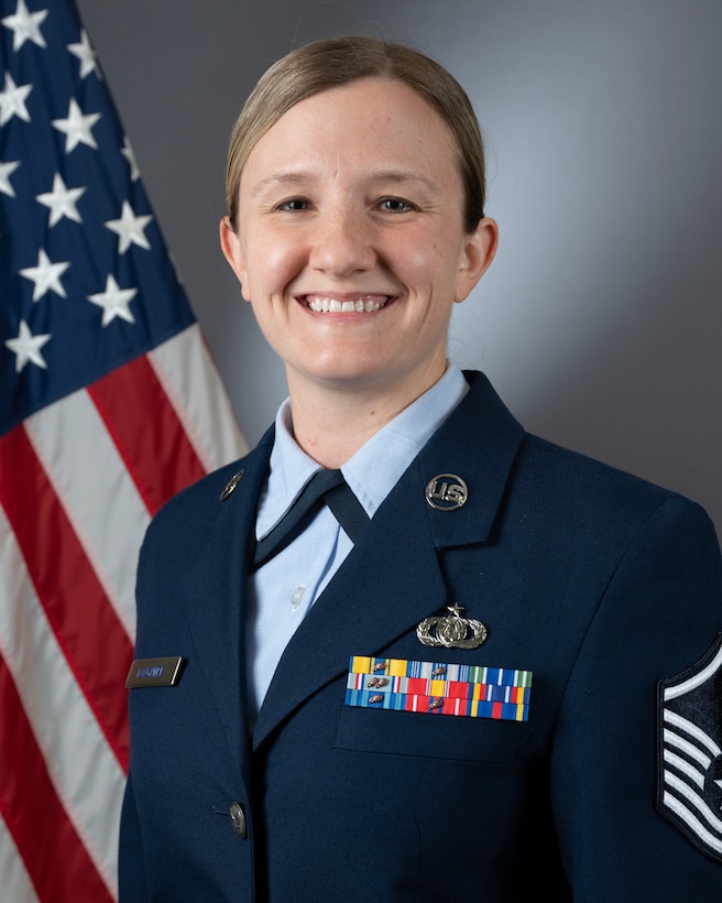 An official headshot of MSgt Kelly Longmire in front of the American flag. She is wearing the blue service dress uniform.