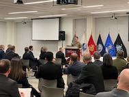 COL Clark speaking at a podium in front of a group of a seated audience