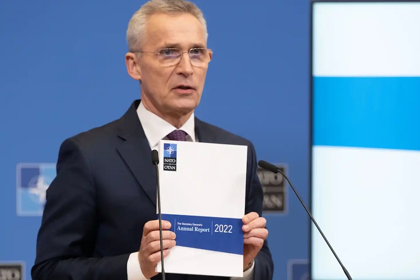 A man stands behind a lectern and holds up a copy of a report.