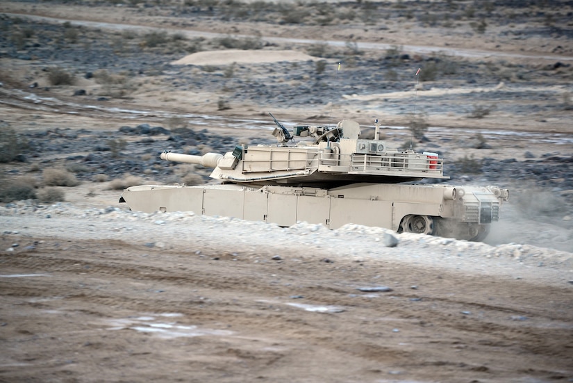 A tank rolls along in a dusty environment.