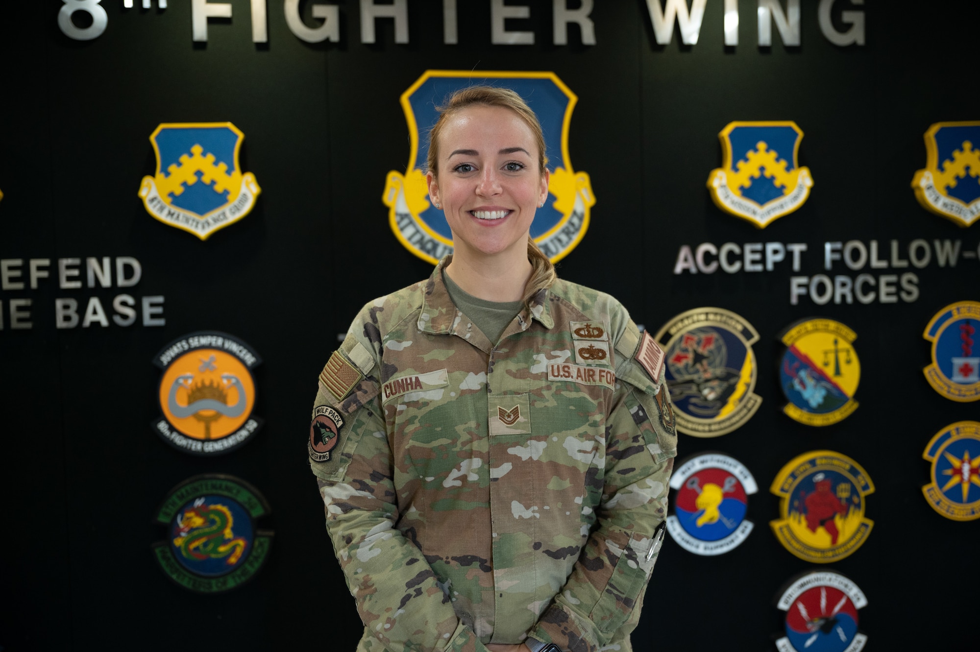 Tech. Sgt. Tiffany Cunha, 8th Fighter Wing command chief executive assistant, stands in front of the 8 FW patch wall inside the headquarters building at Kunsan Air Base, Republic of Korea, Mar. 16, 2023.