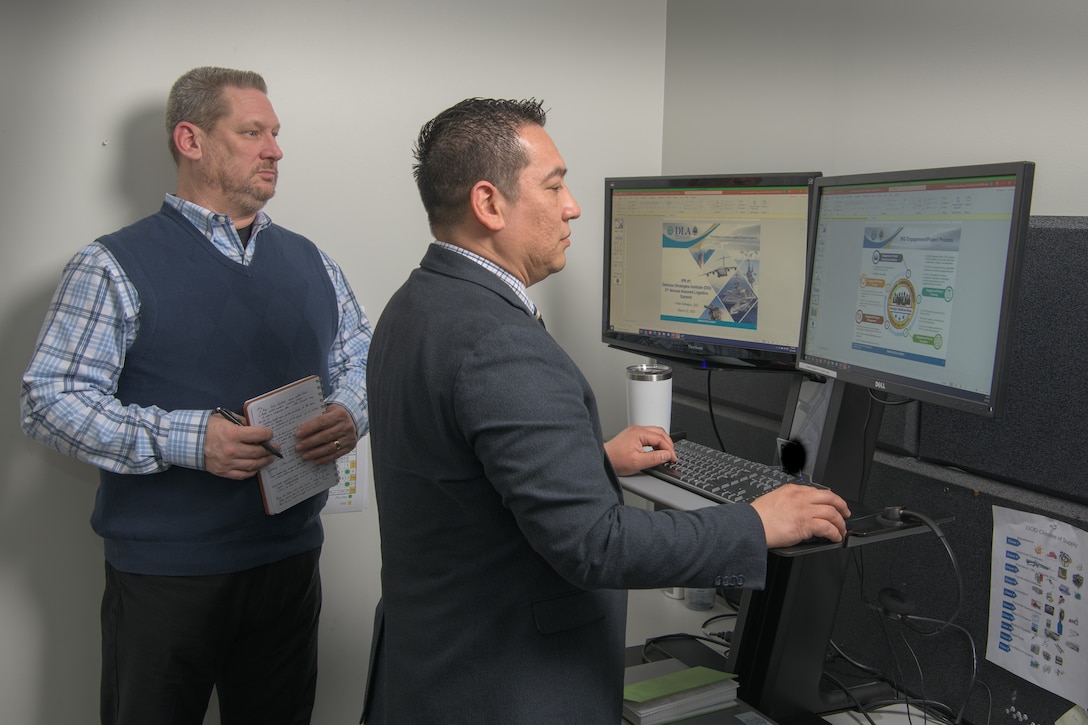 Doug Perezsalgado and Robert Hughes view presentations across two monitors from a standing desk