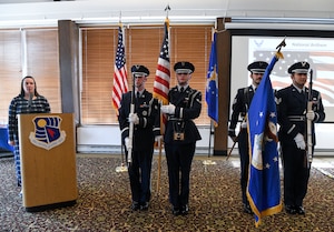 Honor guard carrying U.S. Air Force flag and U.S. flag and guarding them while woman standing behind lectern sings