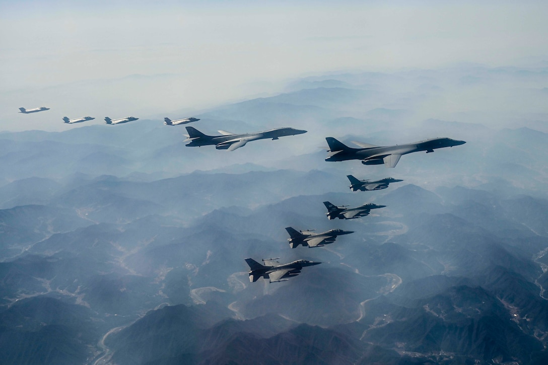 Aircraft fly in formation over a large body of water.