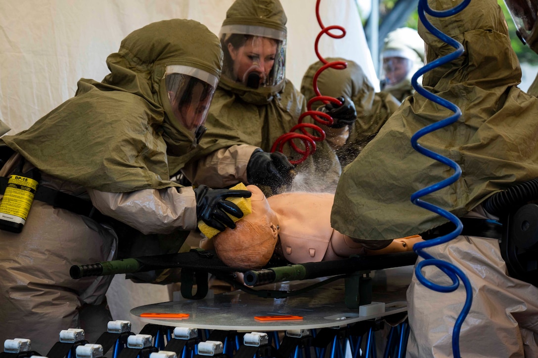 Airmen in personal protective equipment wash a mannequin.