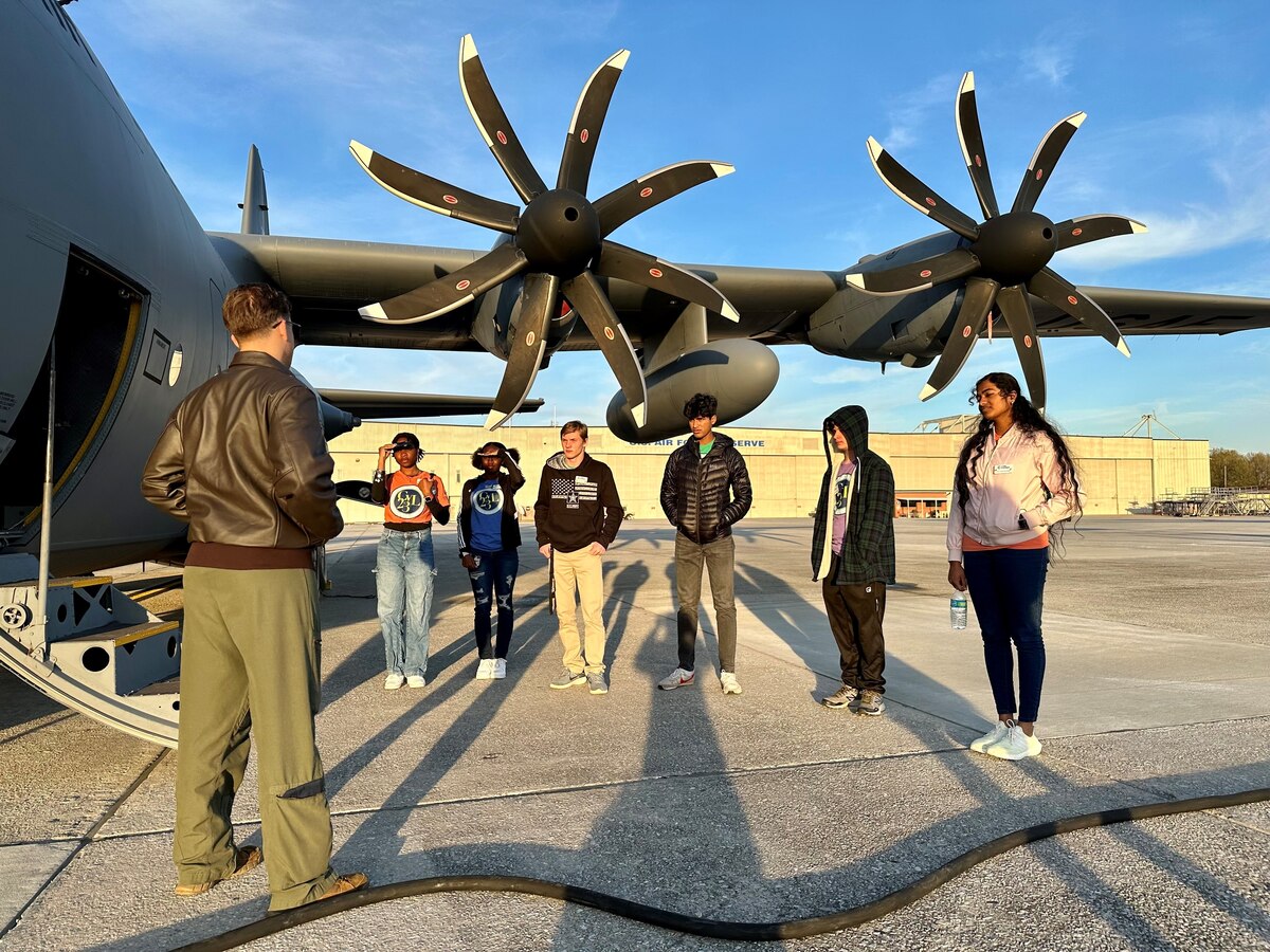 a military member speaks to a group of students standing next to an aircraft