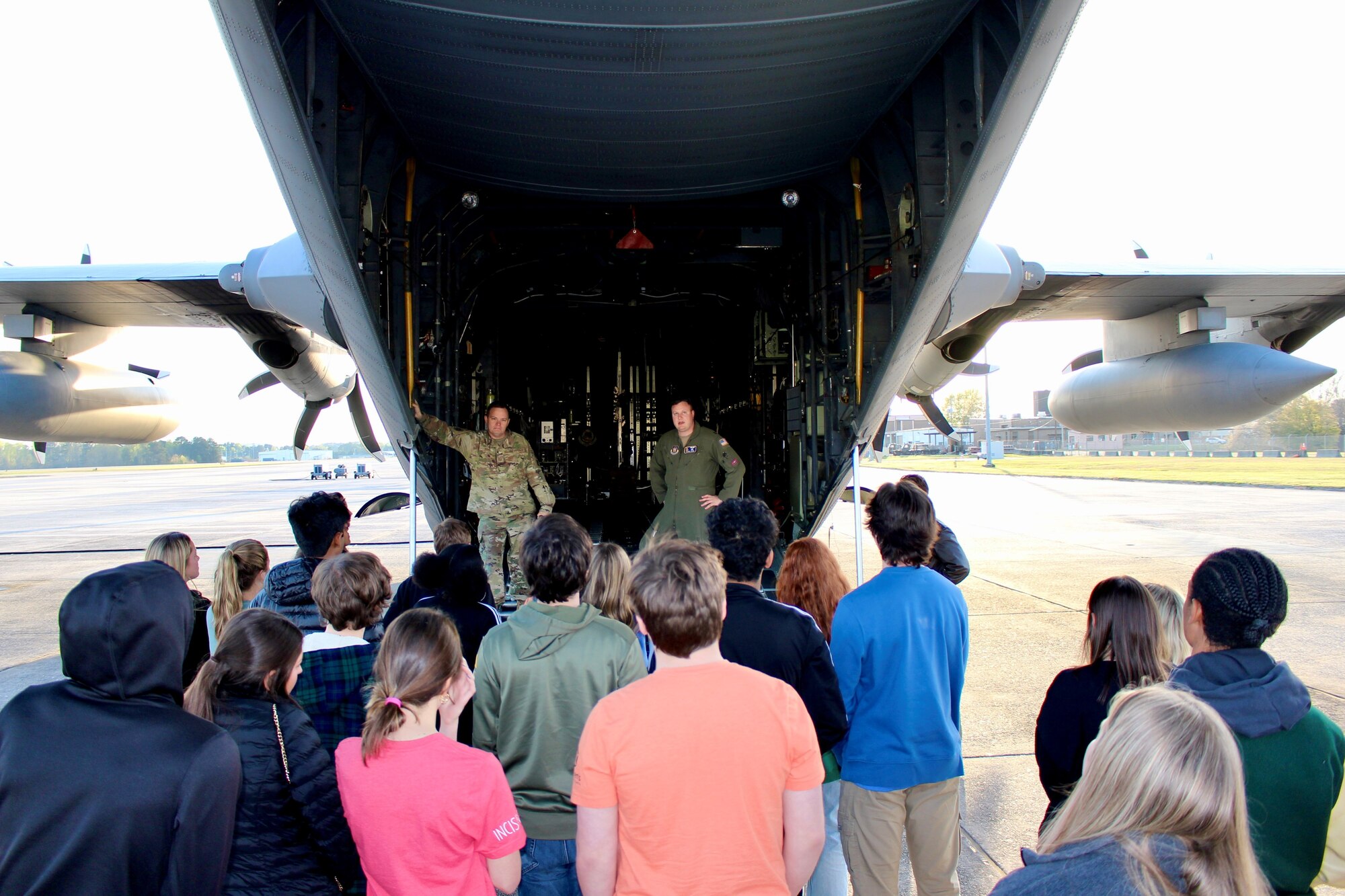 military members stand inside a military aircraft as a group of students looks on