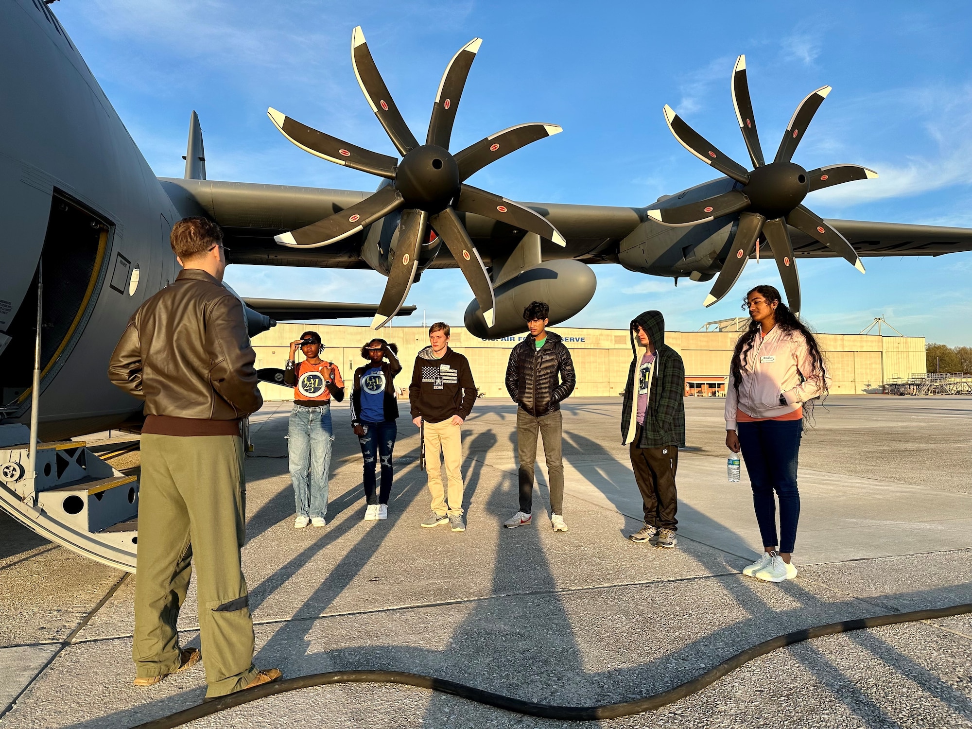 a military member speaks to a group of students standing next to an aircraft