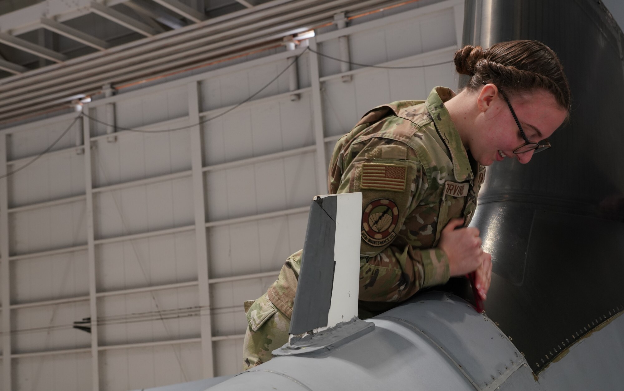 Female Airman removes sealant around panel on aircraft.