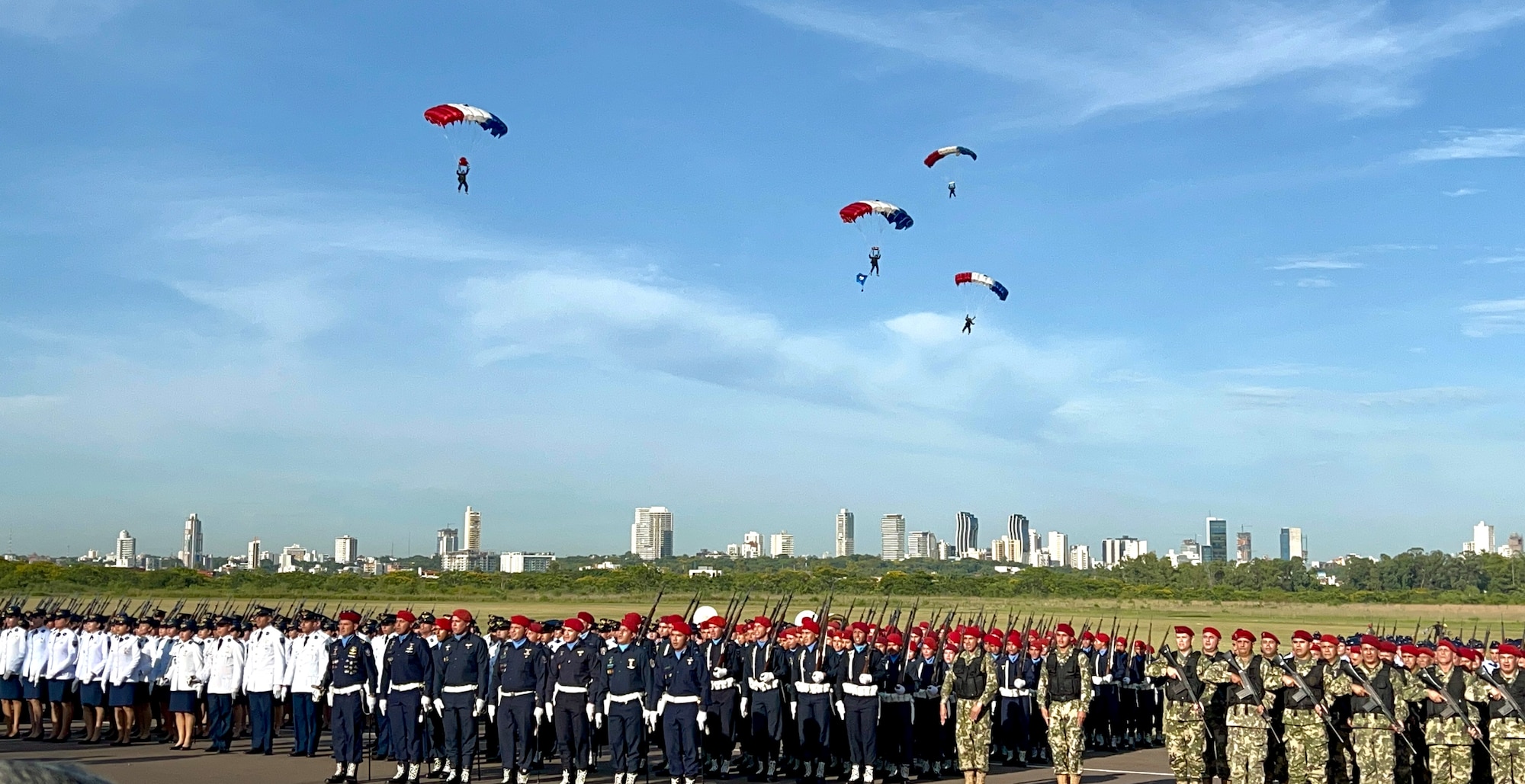 Military members parachute into the Central Ceremony of the Centennial Paraguayan Military Aviation while military members stand at attention in Asunción, Paraguay, Feb. 22, 2023. Senior leaders from 10 countries attended the event to honor Paraguayan Air Force’s Centennial Anniversary. (Courtesy photo)