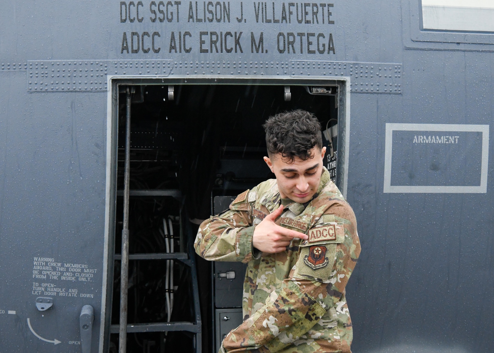 A man in uniform stands in front of a plane, pointing at a patch on his sleeve.