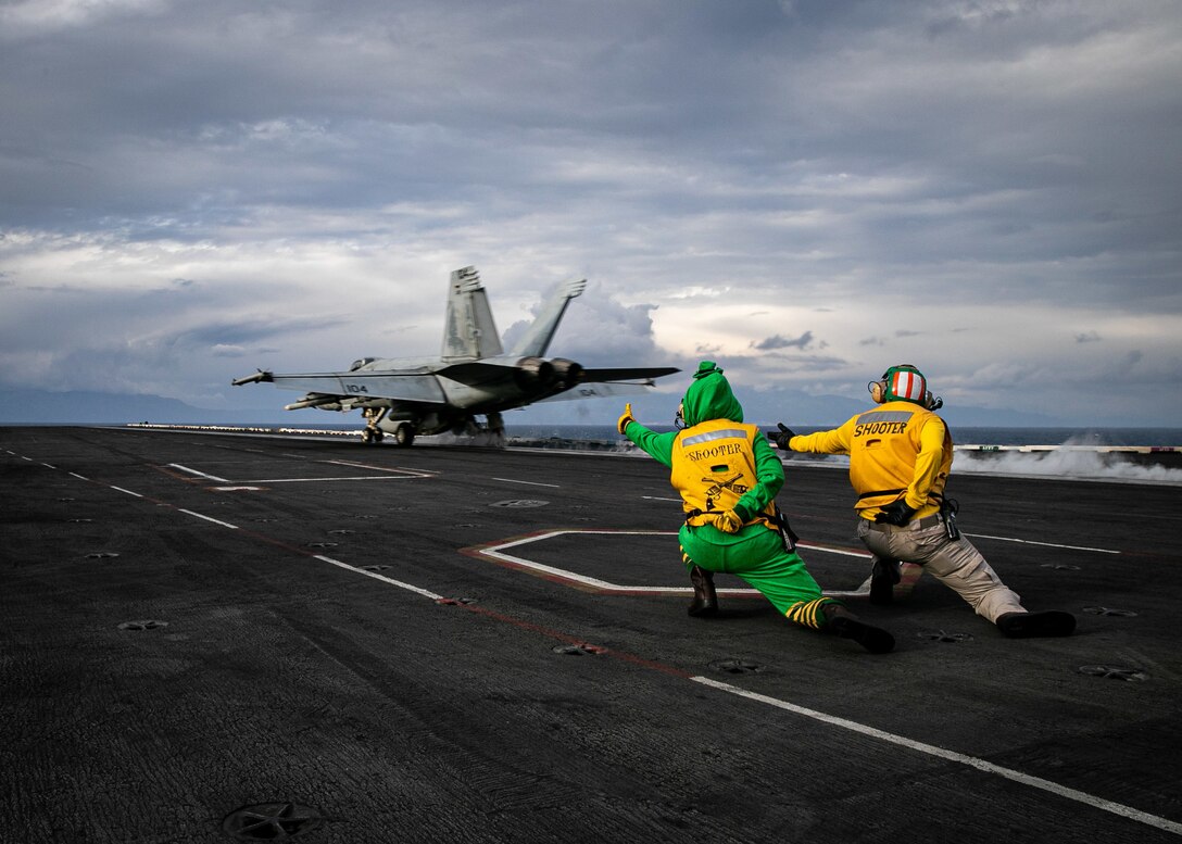 Two sailors give hand signals to help launch a plane from the flight deck