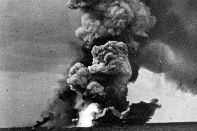 Massive plumes of smoke rise from a ship on the water.