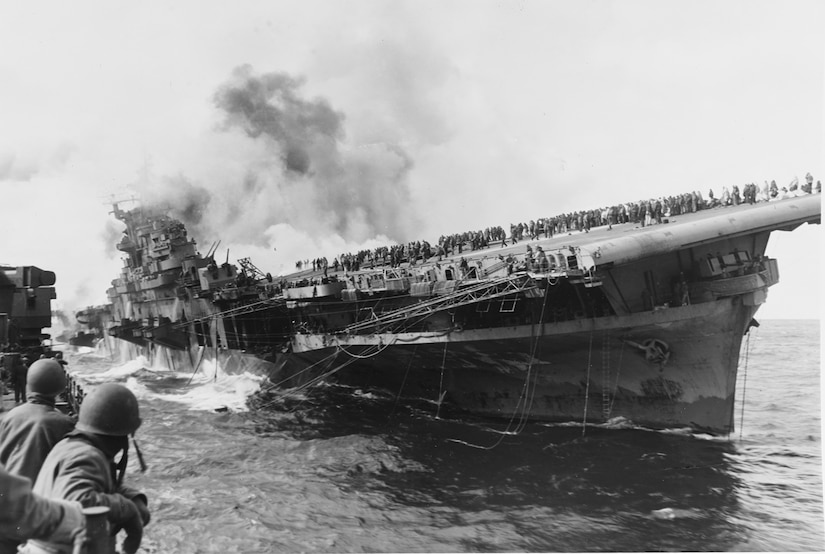 A massive ship lists to starboard in waters as a few men on another ship watch.