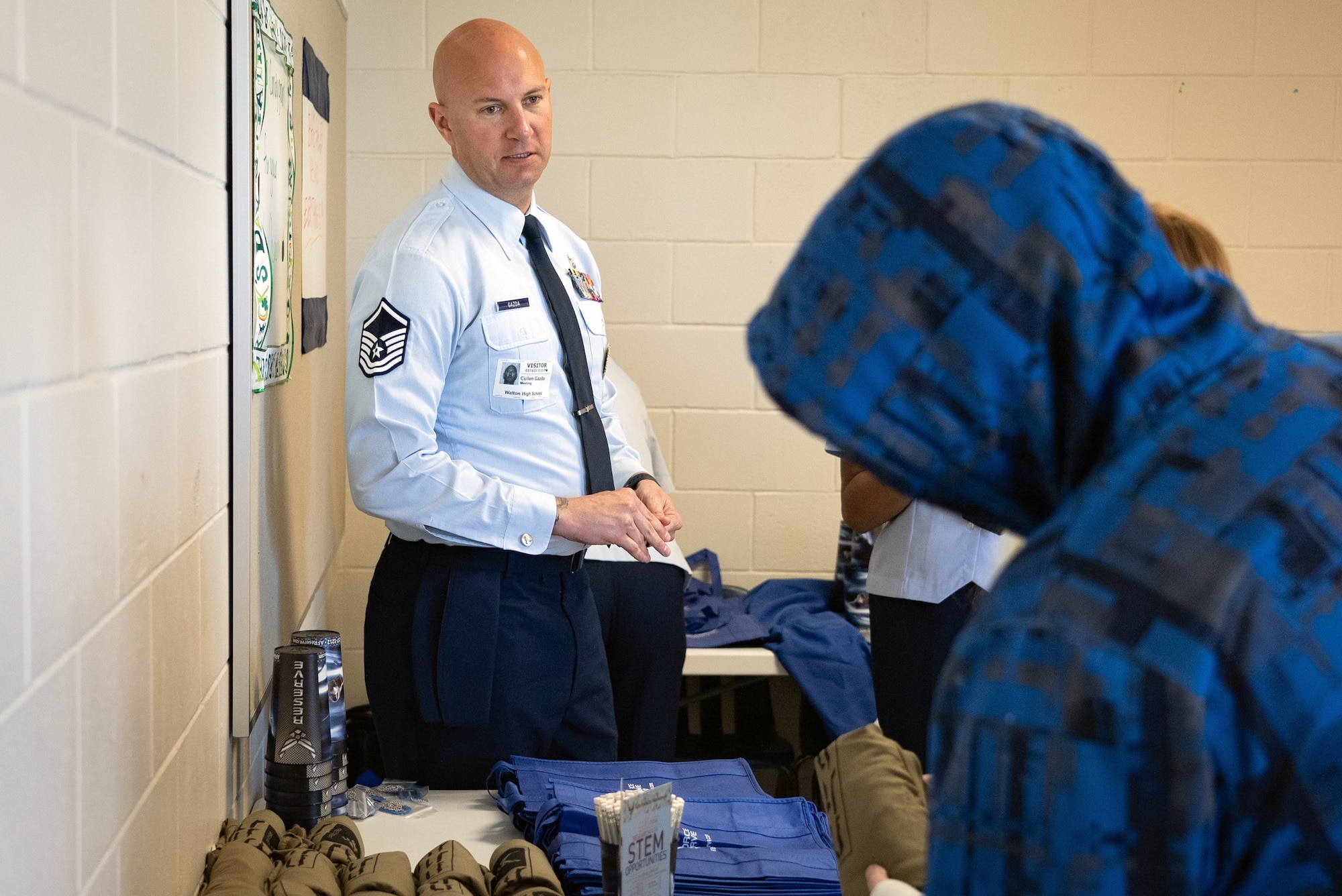 Air Force military member looks over at a high school student in a hoody browsing Air Force items at a recruiting event