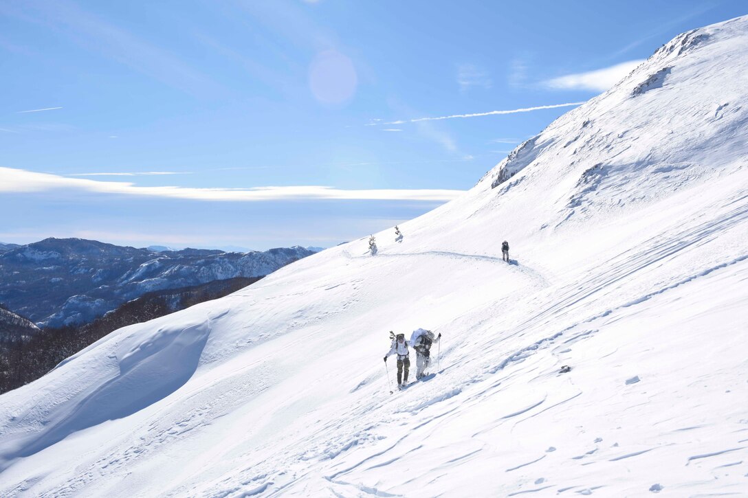 Soldiers hike a snow-covered mountain.