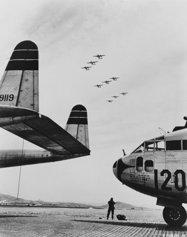 An Airman of the 315th Air Division at Taegu, Korea, stands in front of one of the C-119 ‘Flying Boxcar’ aircraft used to drop Army paratroopers into Munsan-Ni for Operation TOMAHAWK, 23 March 1951.  120 C-119s and C-46 aircraft participated in the airdrop.  (National Archives)