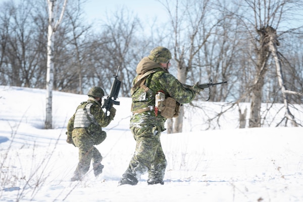 Soldiers with guns move across a snow-covered hill dotted with leafless trees.