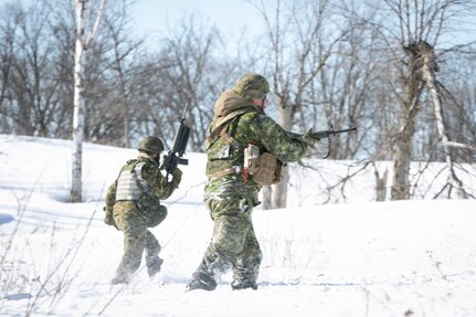 Soldiers with guns move across a snow-covered hill dotted with leafless trees.