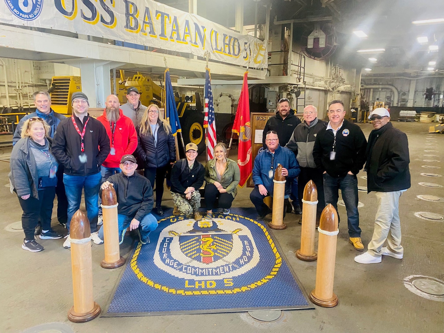 A large group of smiling people on board an Navy ship pose for the camera.