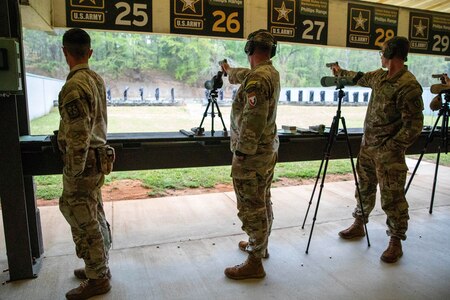 Men in U.S. Army uniforms firing pistols on indoor pistol range.