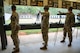 Men in U.S. Army uniforms firing pistols on indoor pistol range.