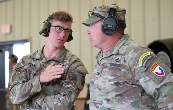 Men in U.S. Army uniforms talking on indoor pistol range.