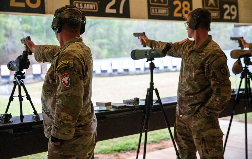Men in U.S. Army uniforms firing pistols on indoor pistol range.