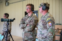 Multiple men in U.S. Army uniforms on indoor pistol range.