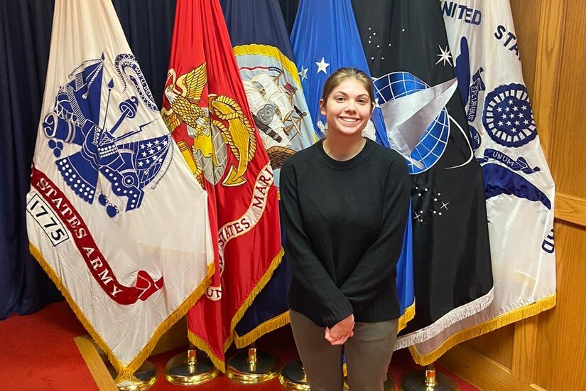 Woman stands in front of flags, smiling.