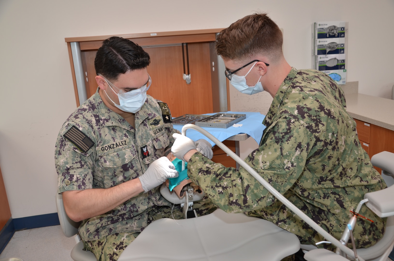 Petty Officer 1st Class Caleb Gonzalez, left, an instructor in the Navy dental assistant program at the Medical Education and Training Campus, Joint Base San Antonio-Fort Sam Houston, Texas, acts as a dentist while training a student in the dental assisting lab. Gonzalez, an instructor in the program, will realize a childhood dream when he begins dental school this summer.