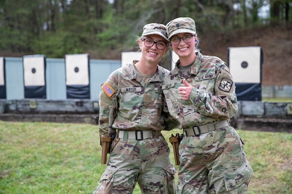 Women in U.S. Army uniform standing in front of outdoor pistol targets.
