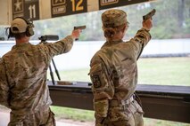 Women in U.S. Army uniforms firing pistols on indoor pistol range.